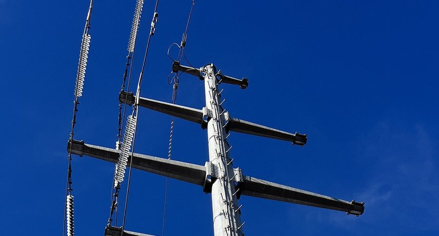 Close view of a pole head showing three cross-arms; the left arms carry insulator strings and conductors, the right arms are bare.