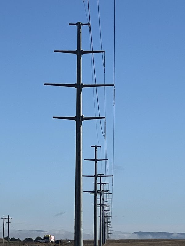 Galvanised steel poles with three cross-arms each, receding into the distance, with a timber distribution pole at lower left.
