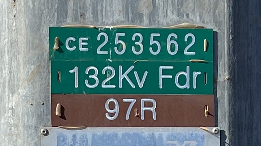Close view of a green and brown asset plate on a galvanised steel pole reading C E 253562, 132 kilovolt feeder, 97R.