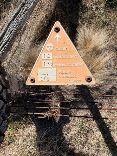 An older orange triangular Telecom Australia marker reading cable 1.2 metres deep, route direction 205, marker type QNP-9C.